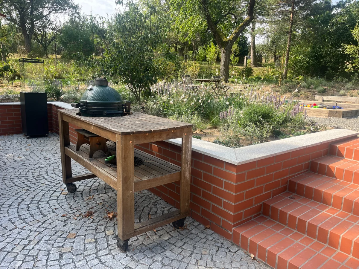 Keramický gril Big Green Egg ve venkovní sestavě s cihlovou zídkou a schodištěm.